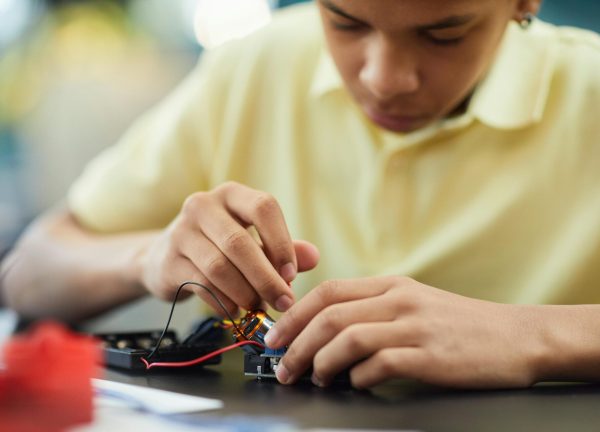 Close-up of a teenager building a robotics project, focusing on electronics and repairs.